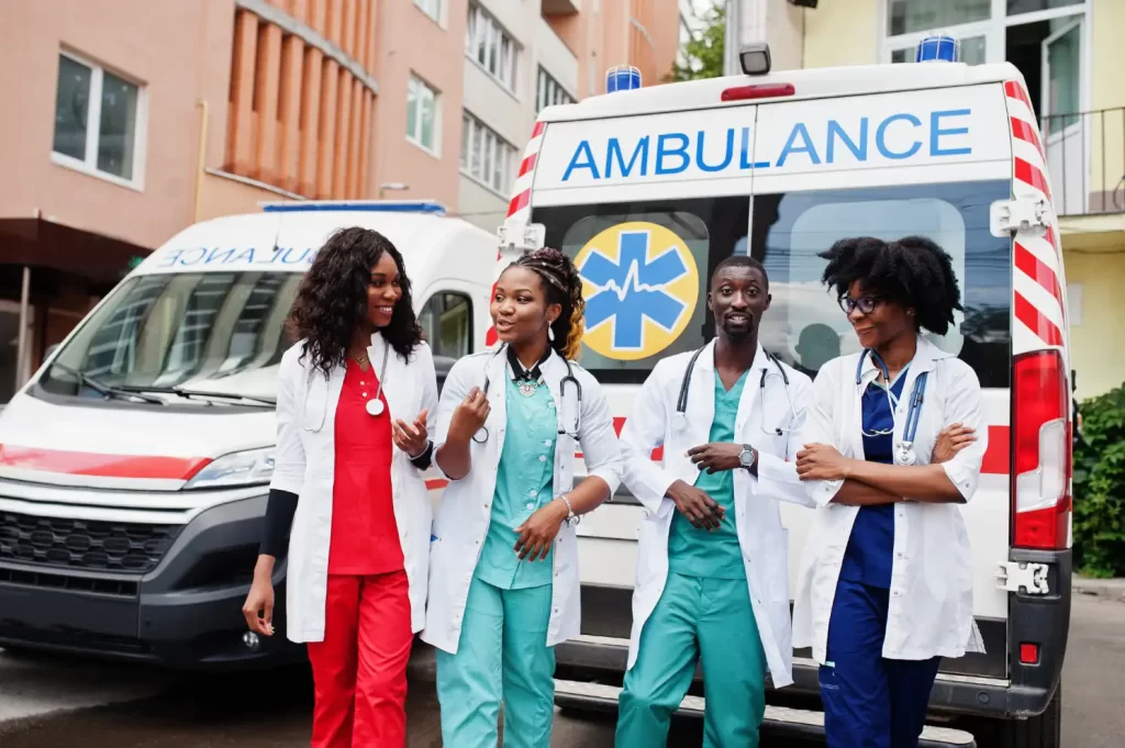 Four pediatric travel nurses from different cities are talking to each other in front of an hospital building and ambulance