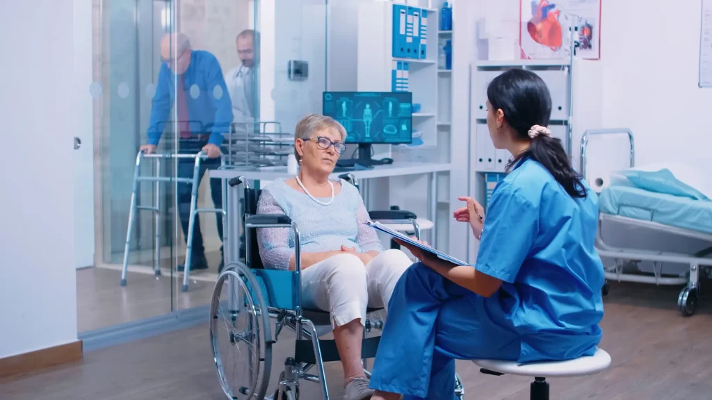 Nurse giving advice to her aged woman patient with walking disabilities sitting wheelchair into private modern recovery clinic
